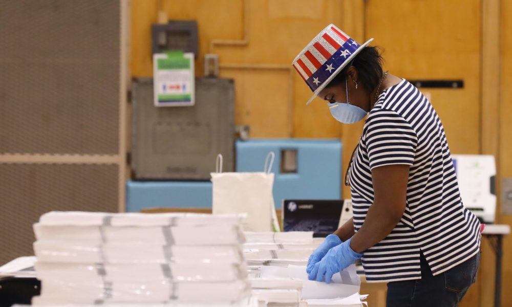 COVID-19大流行期间，一名戴口罩的投票工作人员在威斯康星州的一个投票站整理选举材料。