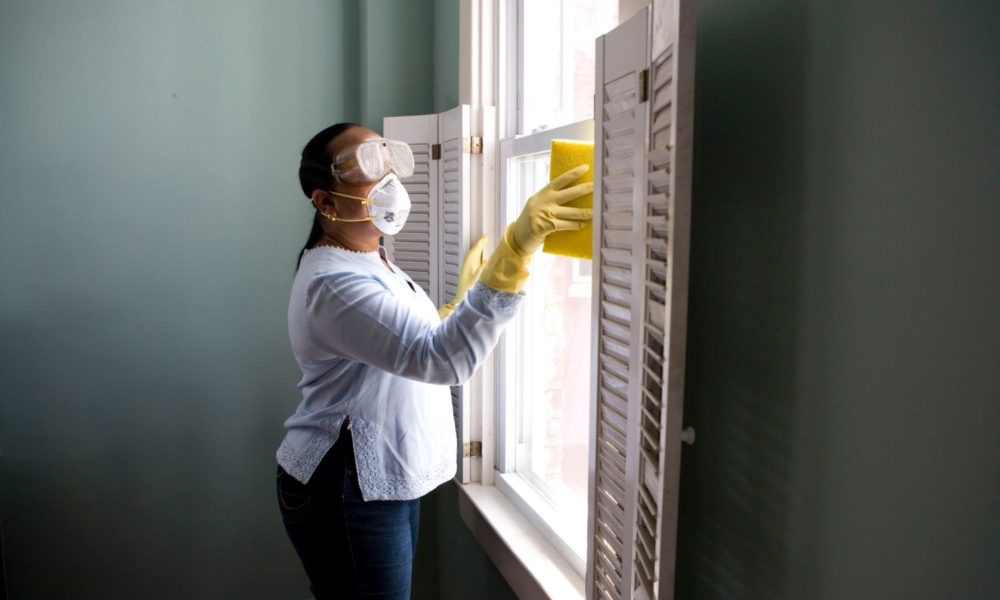 一个女人站在窗前打扫卫生。她戴着防护装备:手套、护目镜和口罩。
