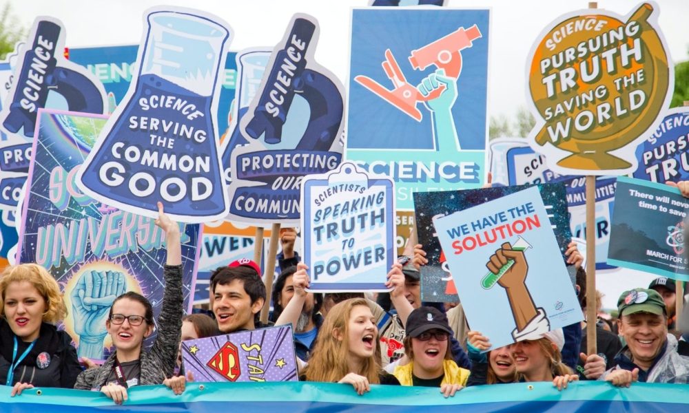 一群科学活动家为科学游行，举着写有“科学家向权力讲真话”和“科学为公众利益服务”的标语。
