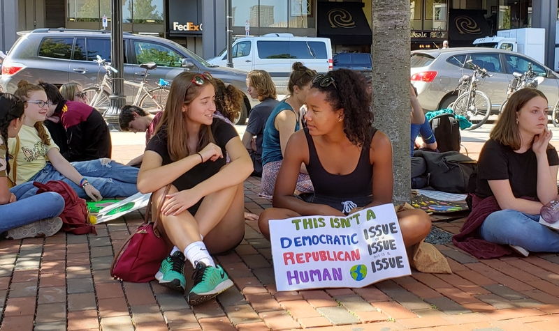 两名年轻抗议者在树荫下休息，他们的标语暗示气候变化不是一个党派问题。