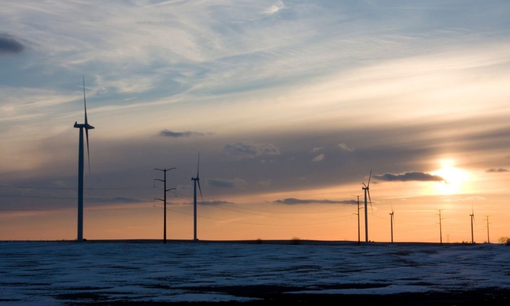 伊利诺斯州中部风电场的一些风力涡轮机的镜头，在一个寒冷的冬季傍晚日落时，涡轮机周围可见雪