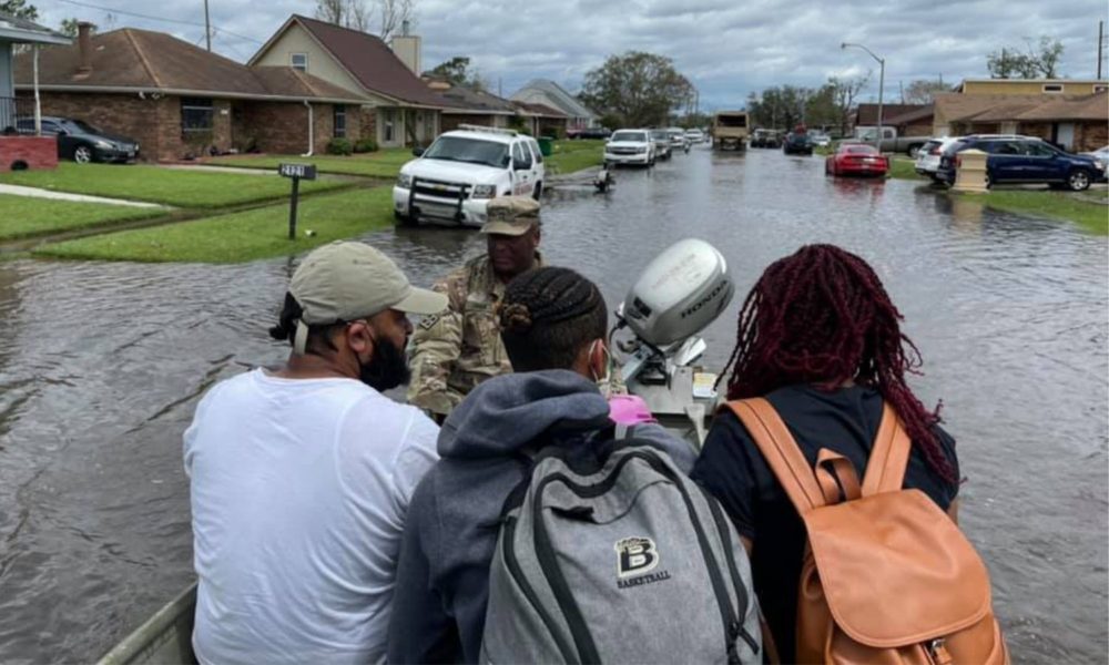 三个人坐在一艘由一名国民警卫队成员配备的小摩托艇上，将他们从被洪水淹没的社区疏散出去