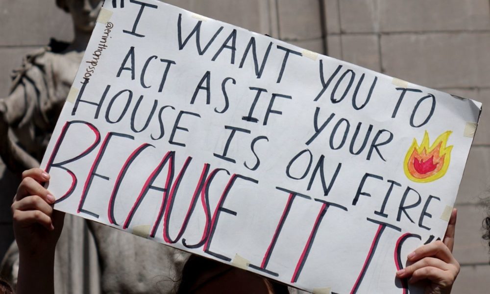 在纽约的一场青年气候抗议活动中，一双手举着一个牌子，上面写着“我希望你表现得像你的房子着火了一样，因为它确实着火了”