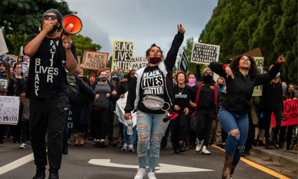 一群看起来很年轻的人穿着“黑人的命也重要”t恤，举着“黑人的命也重要”的牌子，和平地沿着街道游行