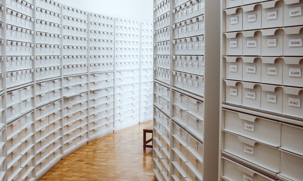 这张照片是一堆看似无穷无尽的白色记事本，比一个人还高，伸展在木地板的两侧——暗示着档案