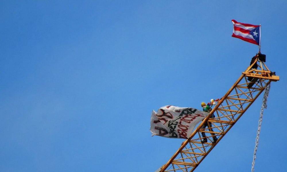2007年11月14日，波多黎各活动家Tito Kayak爬上圣胡安Paseo Caribe项目的建筑起重机，并在圣胡安一个新度假村的工地上停留了一周，抗议其建设。这是一张蓝天的照片，前景是一架黄色的建筑起重机，激进分子蒂托·皮艇站在起重机上，波多黎各国旗在顶部飘扬。