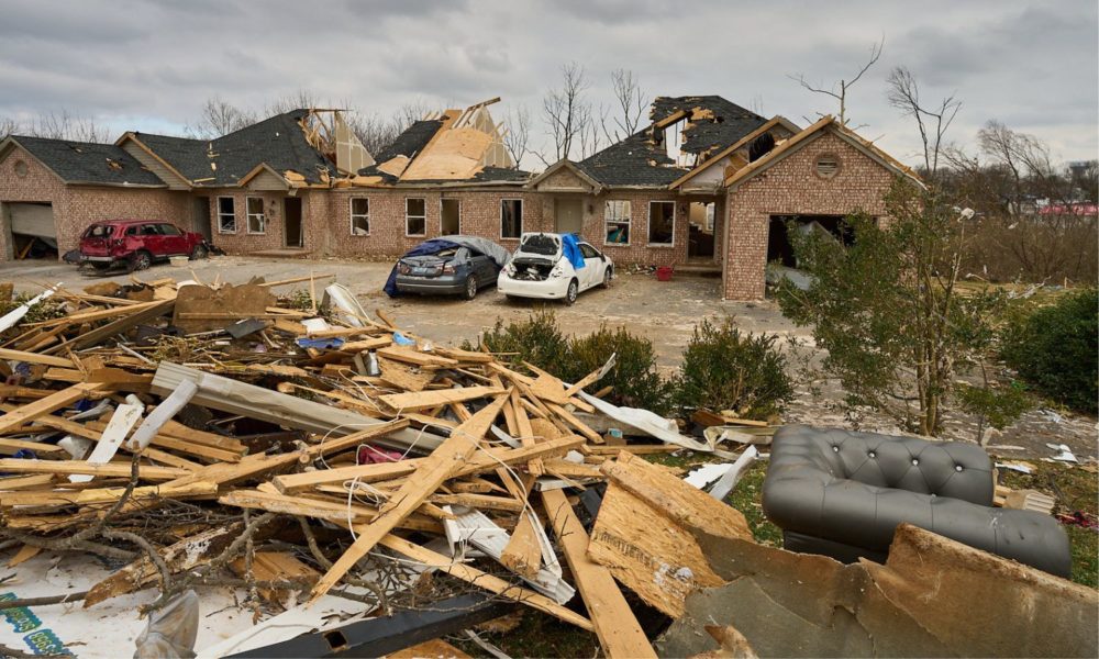 这是肯塔基州鲍灵格林被破坏的场景，前景是一堆瓦砾，包括一个沙发，背景是一个被摧毁的房子