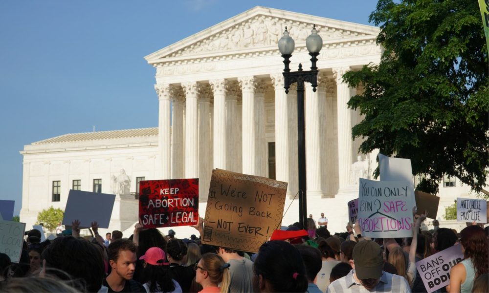 抗议者在华盛顿最高法院大楼前举着标语，其中一个写着“我们不会回去”。