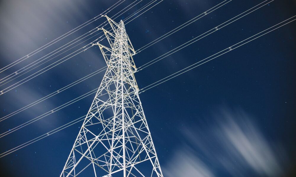 在这张低角度的输电塔照片中，可以看到蓝天，在前景中，一座白色的输电塔连接着电线