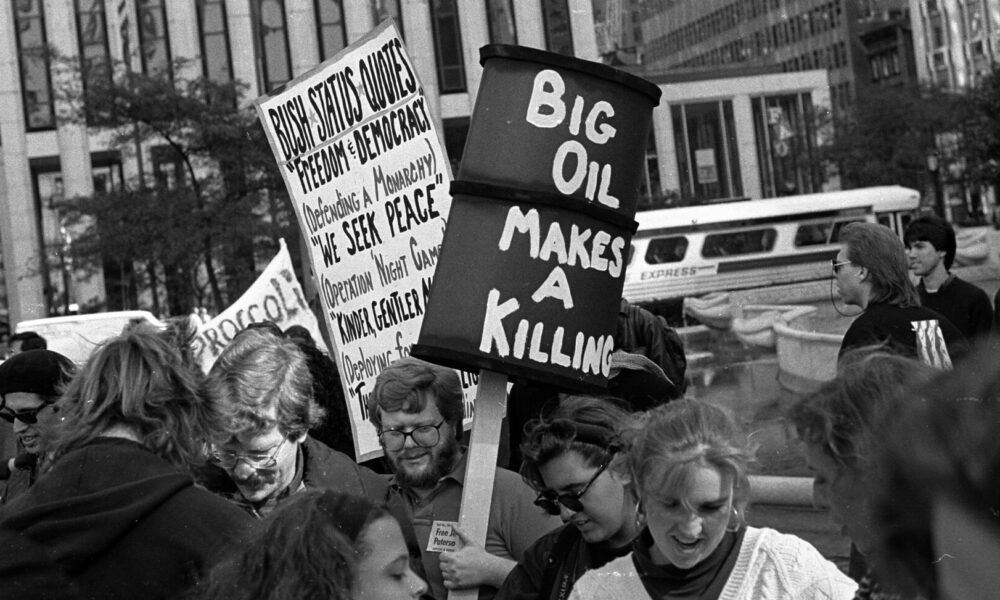 黑白照片，人们在纽约市街头举着标语，其中一个写着“石油巨头赚大钱”。