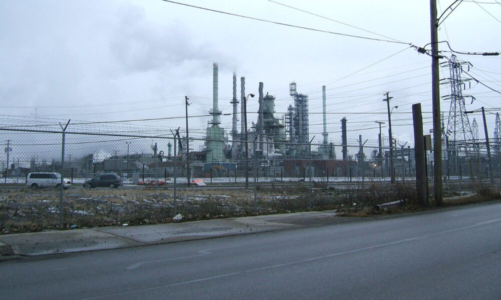 灰色的天空与密歇根州底特律一家石化厂排放的烟雾混合在一起，透过链式围栏可以看到