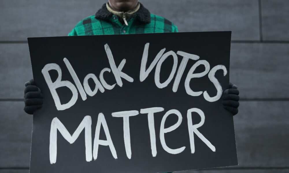 一名男子举着一个牌子，上面写着“黑人投票很重要”