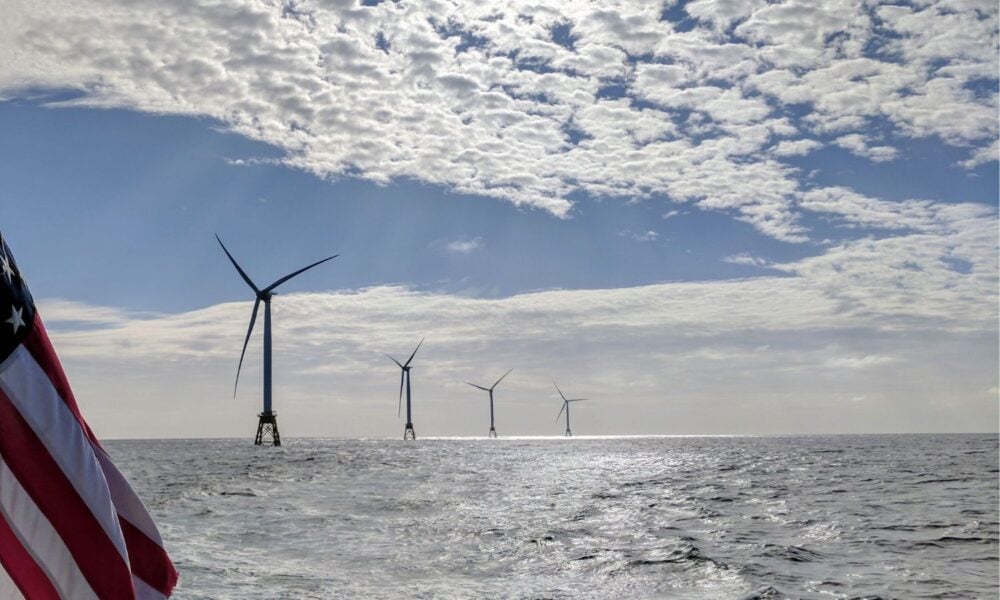 A bright, sunny day on the open ocean: a line of offshore wind turbines is visible along with an American flag, presumably mounted on a boat