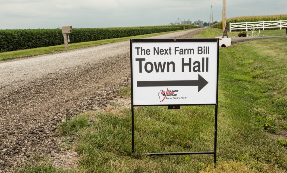 乡村道路旁的标志照片。上面写着“下一个农业法案”，下面写着“市政厅”，还有一个箭头指向远离道路的方向。
