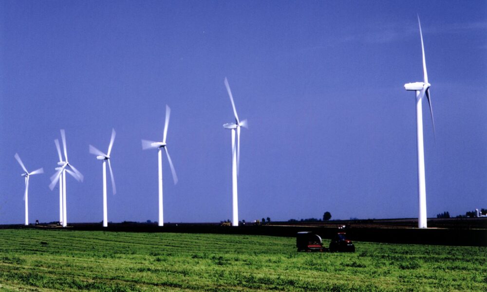 photo of a series of wind turbines against a blue sky, with a green farm field below