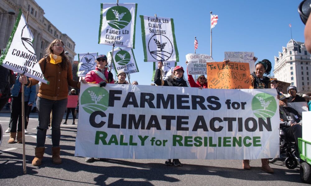 一群人在华盛顿举行的集会上举着横幅，上面写着“农民为气候行动:为恢复力而集会”。