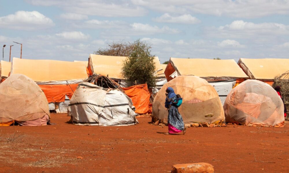 一名背着背着孩子的妇女走过索马里的一个难民营，在那里，灾难性的干旱造成了100多万难民