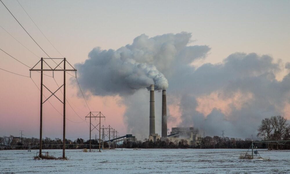 在粉色的天空和蓝色的水的背景下，污染的云团在明尼苏达州一家发电厂的两个烟囱上翻腾