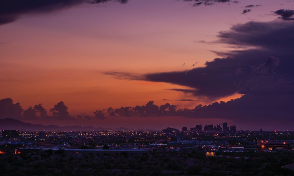 The Phoenix skyline at sunset, with a beautiful orange sky contrasting with dark clouds overhead
