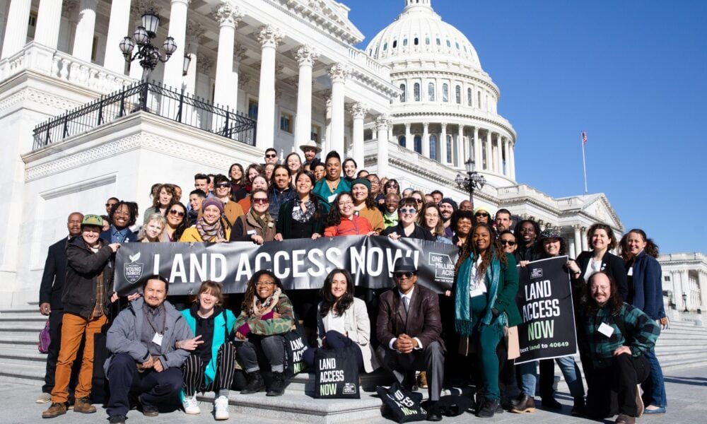 photo of a large group of people posed at the base of the US Capitol's steps, with the dome behind them, holding a banner that reads 