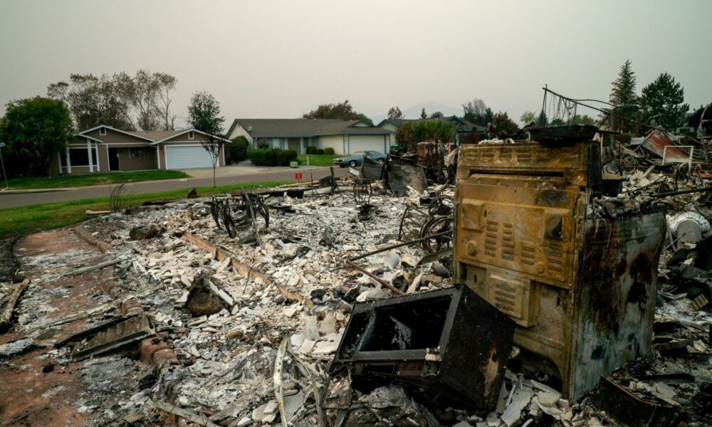 A burnt down house in the foreground, while two houses in the back were untouched by the Carr Fire in Redding California.