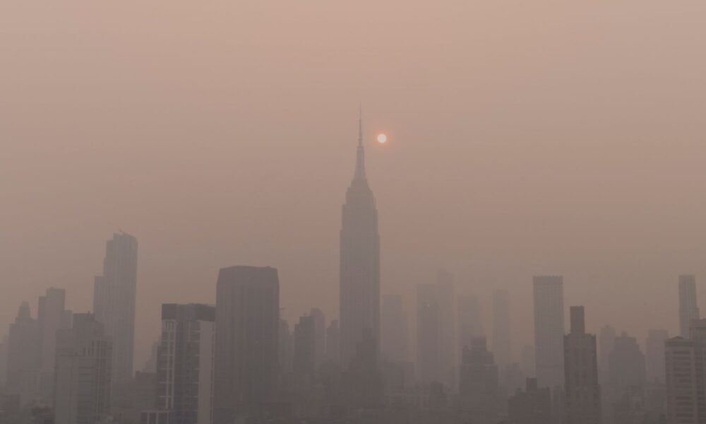日出或日落时的纽约市天际线，2023年6月，加拿大野火带来的淡黄色烟雾掩盖了太阳和清晰的建筑物视野