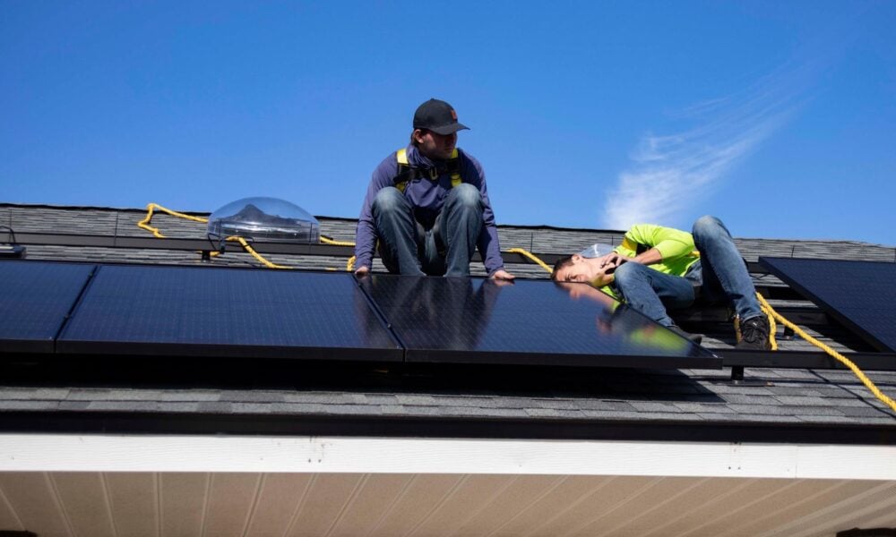 两个白人男子的工作安装太阳能电池板on the roof of a home in St. Augustine, Florida, under a bright blue sky