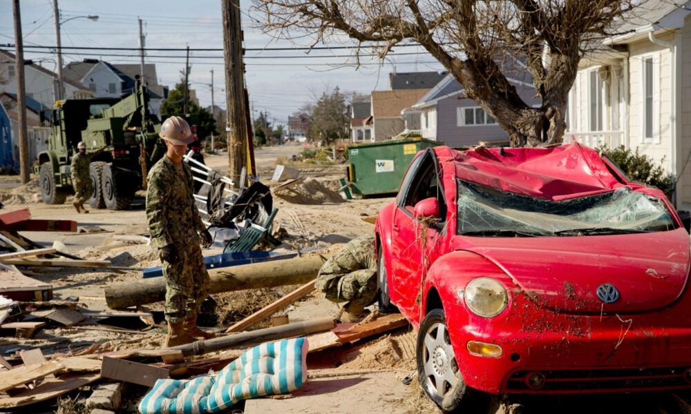 Two US Navy members work to remove a stranded, hurricane-damaged car from wreckage around it, after a big storm.